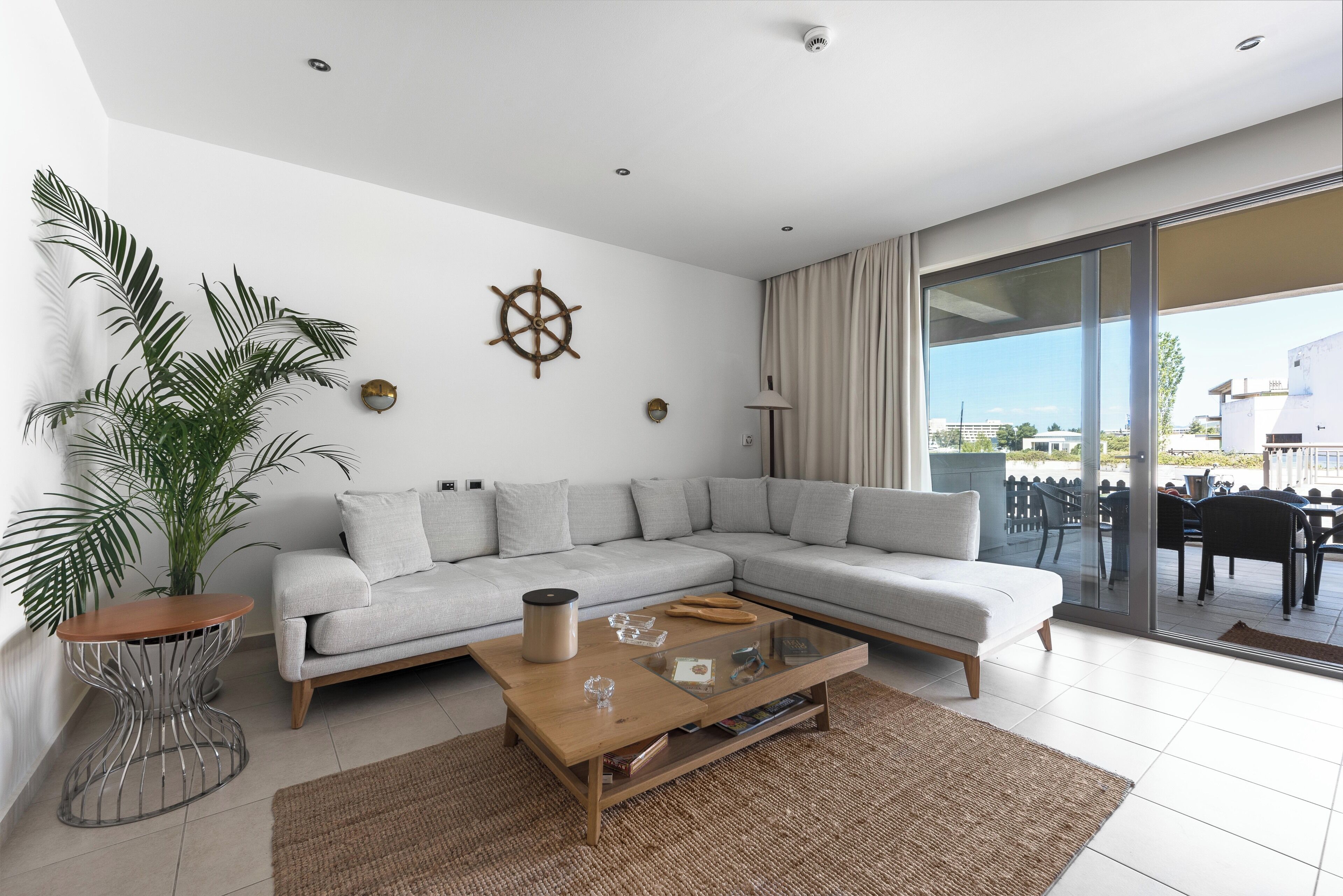 A modern living room with a sectional sofa, a glass coffee table, a potted plant, and a view of the outdoors.