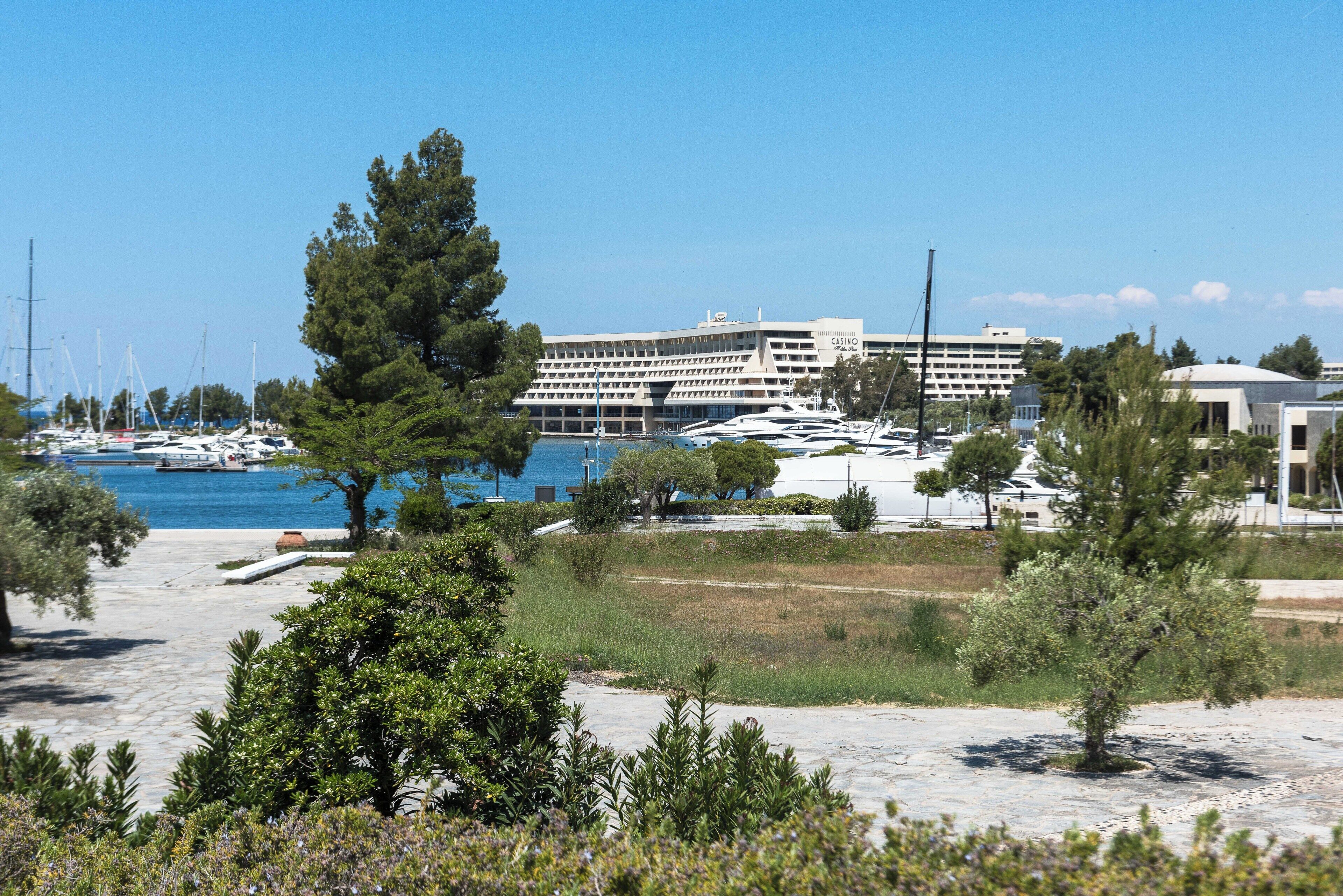 A coastal hotel with multiple floors, a marina with boats, and a large tree in the foreground.