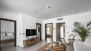 Un salon moderne comprenant un canapé, une table basse, un téléviseur et un coin cuisine visible à travers une porte ouverte.