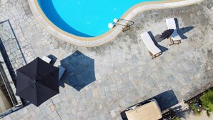 Vue aérienne d’une piscine à bordures incurvées, entourée de carreaux de pierre. On y voit des chaises longues et des parasols.