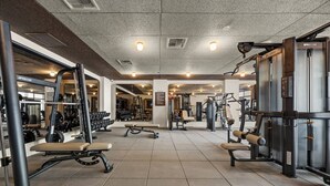 Uma academia com diversos equipamentos de exercícios, bancos e um espelho grande na parede.