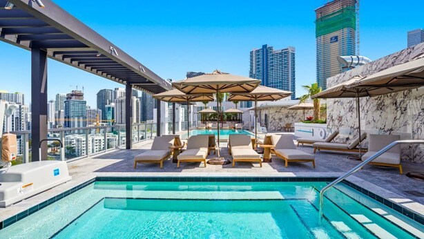 Piscina no terraço com espreguiçadeiras e guarda-sóis, com vista para o horizonte da cidade.