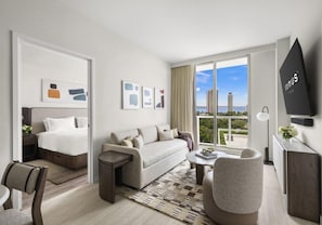 A modern hotel room with a bed, sofa, armchair, and a large window offering a city view. - Domus Brickell Stylish 1BR Condo (Miami)