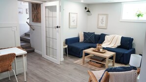 Un salon chaleureux avec un canapé bleu, une petite table, un fauteuil en osier et un escalier menant à un autre niveau.