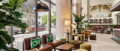 Eine geräumige Lobby mit Sitzbereichen, einem Empfangstresen und einem großen Fenster mit Jalousien.