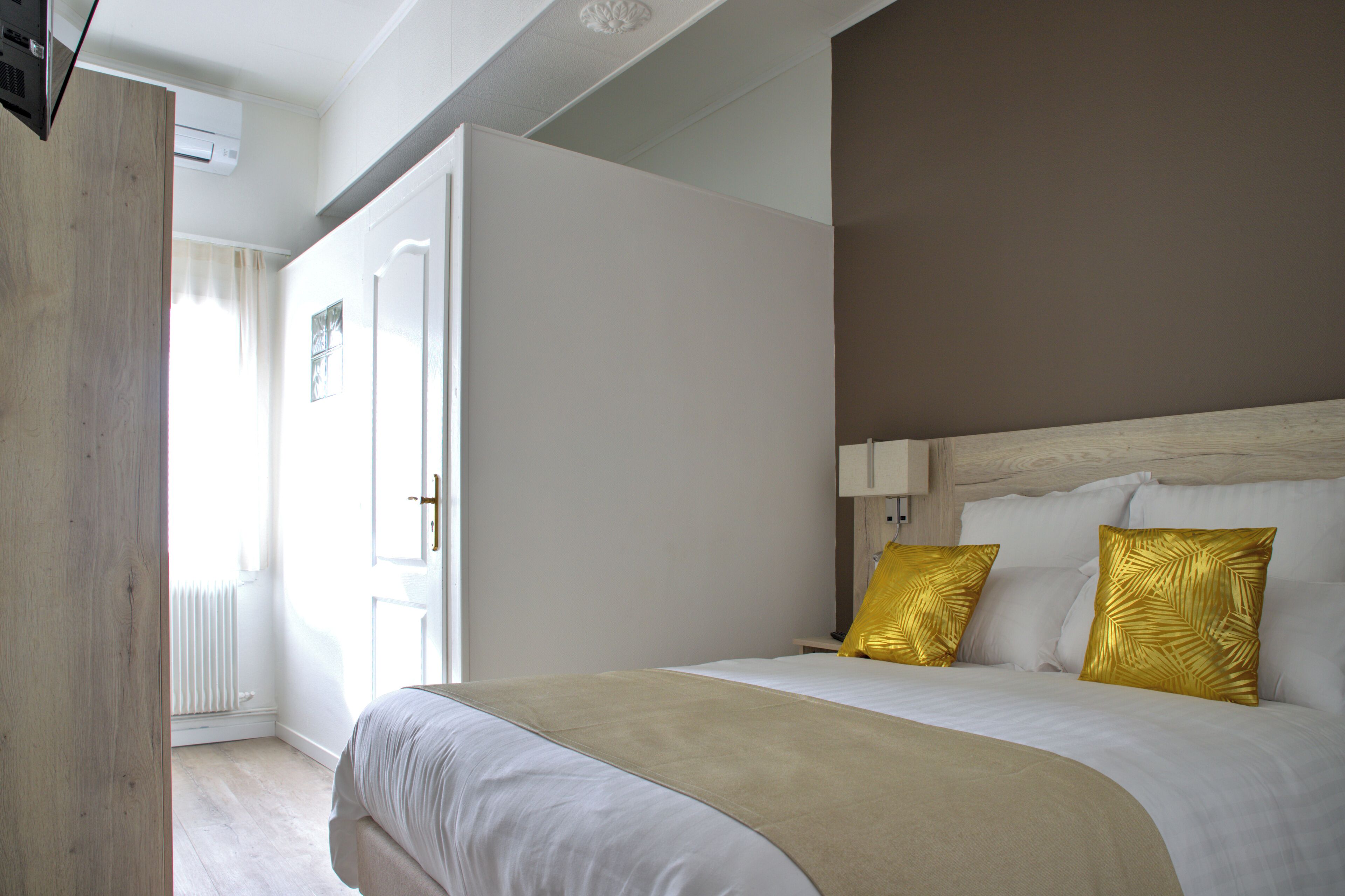 A hotel room with a bed, a wooden wardrobe, a white radiator, and a window with curtains.