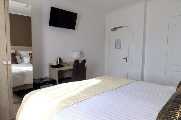 A hotel room with a bed, a desk with a chair, a television mounted on the wall, and a door. - HOTEL ARCHIPEL (Balaruc-les-Bains)