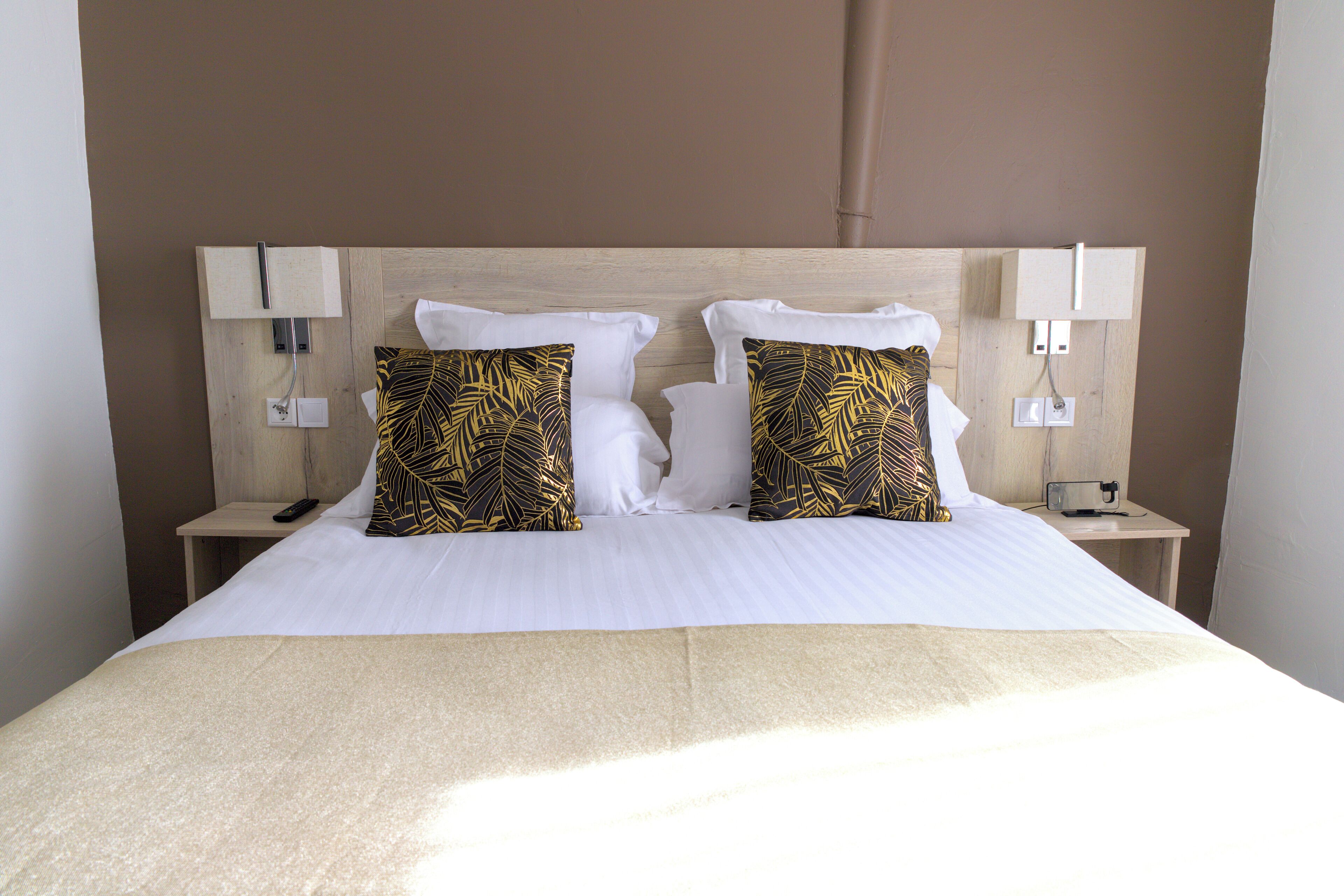 A hotel room with a bed, two nightstands, a lamp, and a power outlet on each side.