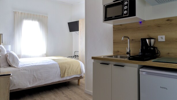 A bedroom with a bed, a bedside table, a TV, and a window with curtains. - HOTEL ARCHIPEL (Balaruc-les-Bains)