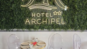 A hotel sign with a neon 'AR' logo and the name 'HOTEL ARCHIPEL'. There is a round table with chairs in front. - HOTEL ARCHIPEL (Balaruc-les-Bains)