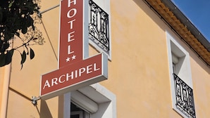 A hotel sign with 'HOTEL ARCHIPEL' written on it, a balcony with black wrought iron railings, and a yellow building facade. - HOTEL ARCHIPEL (Balaruc-les-Bains)