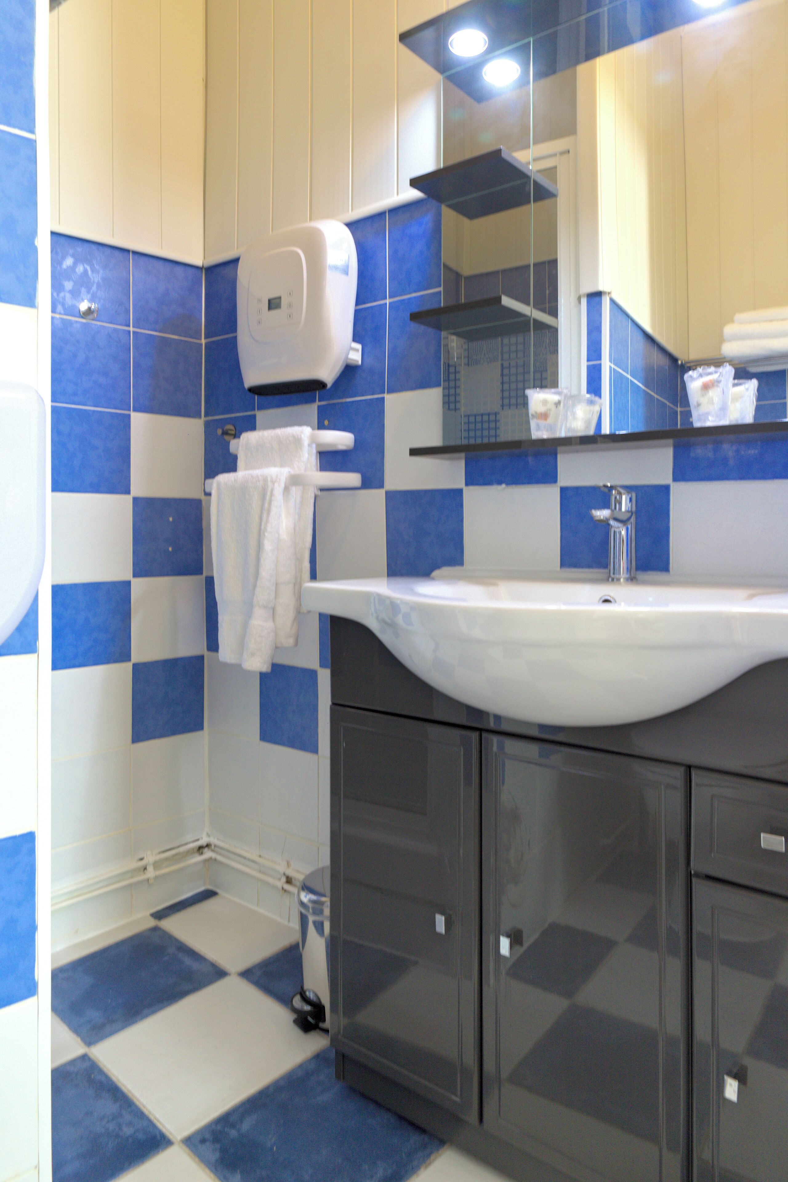 A bathroom with a white sink, blue and white checkered tiles, a towel dispenser, and a mirror above the sink.