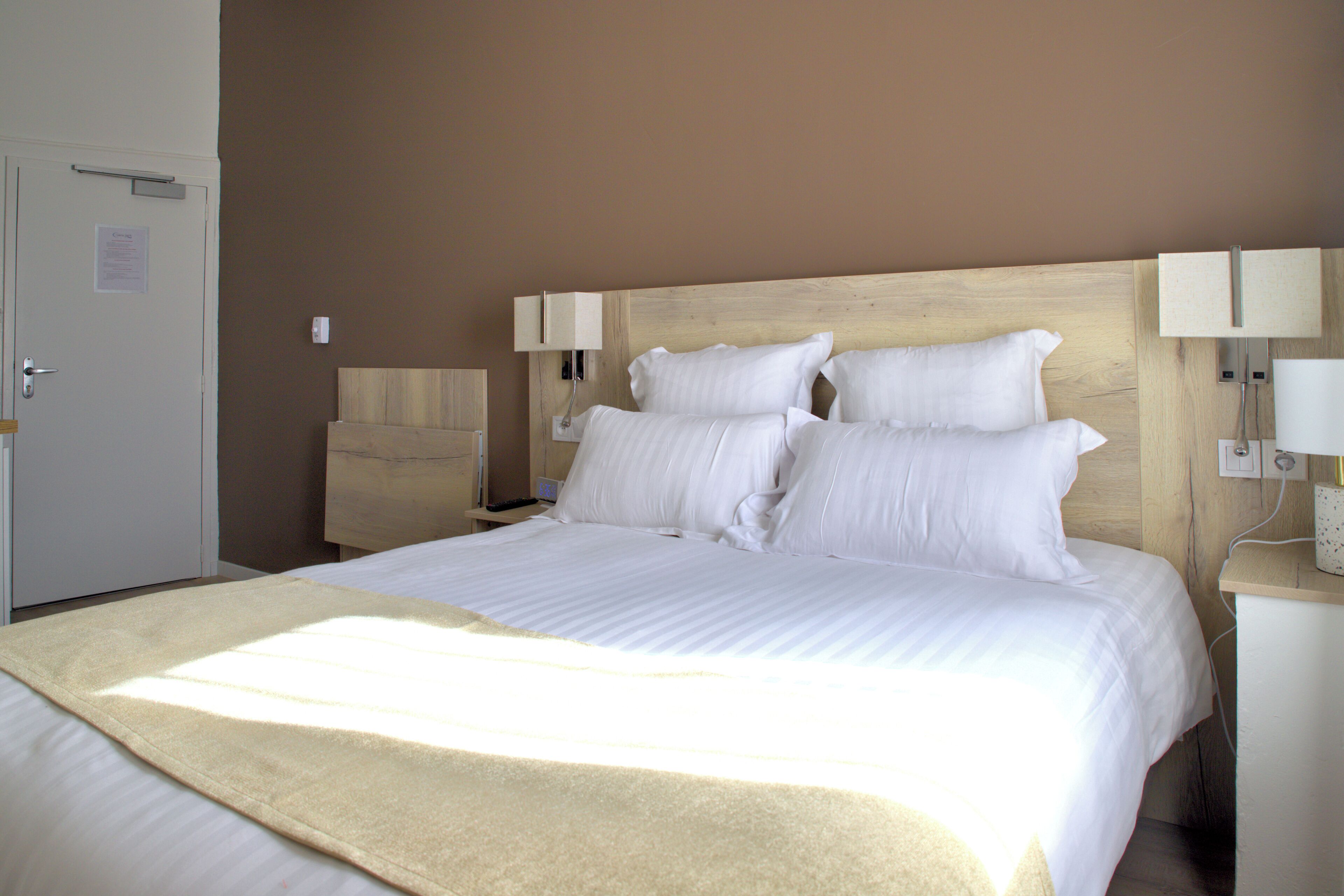 Une chambre d’hôtel avec un grand lit, deux tables de chevet avec des lampes, une porte et un luminaire fixé au mur.