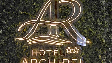 A neon sign with the letters 'AR' and the words 'HOTEL ARCHIPEL' on a wall covered with greenery.