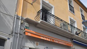 Et hotel med et skilt der viser 'HOTEL ARCHIPEL', en balkon med dekorativt metalværk og en dør med et skilt, der angiver 'HOTEL ARCHIPEL'.
