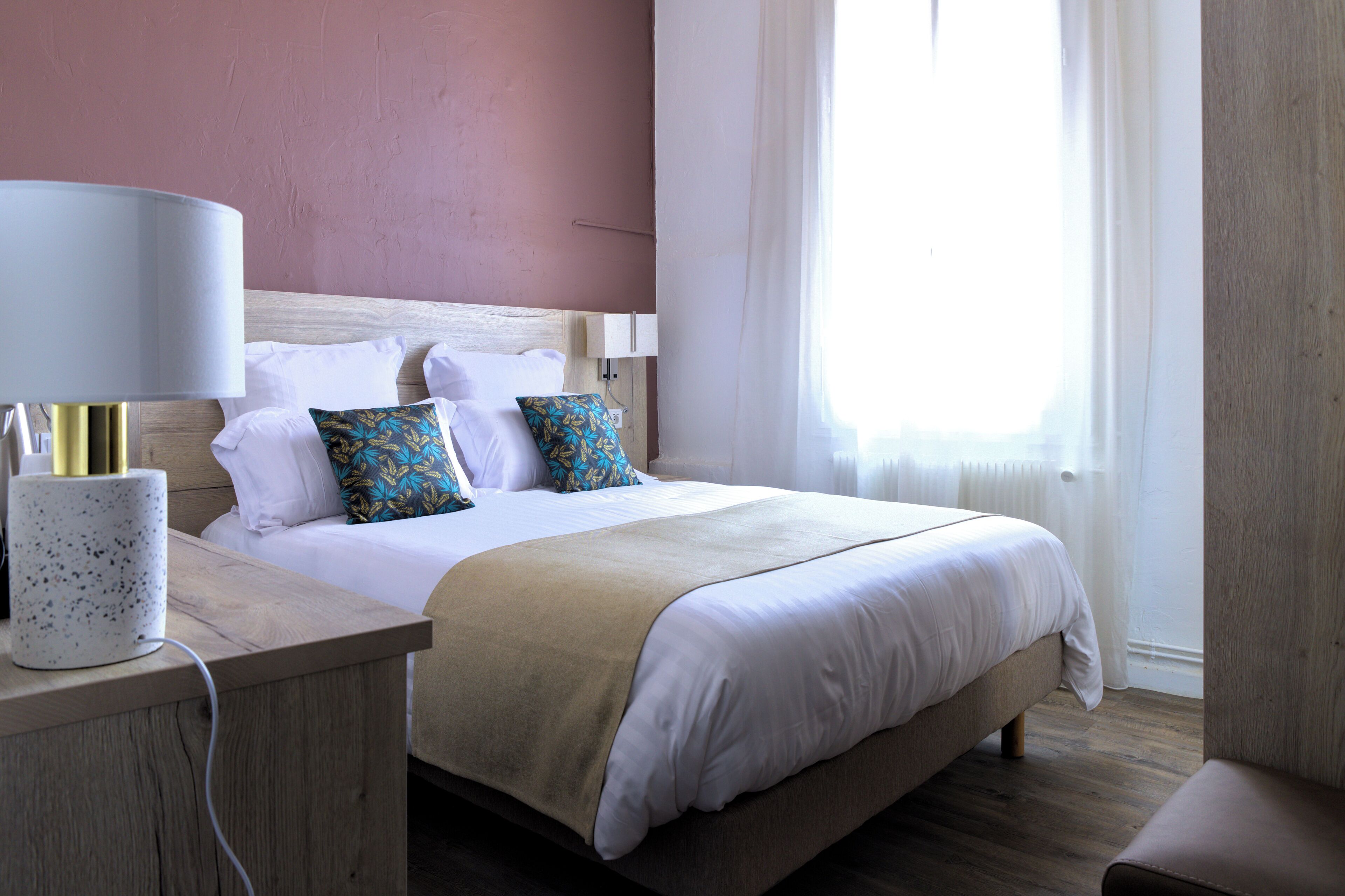 A hotel room with a bed, bedside table, lamp, and a window with curtains.