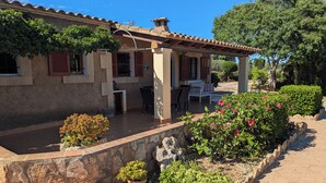 A house with a patio, outdoor seating, and a garden with flowers and shrubs. - Villa with private pool, garden and barbecue close to the beach with WIFI (S'Horta (Felanitx))