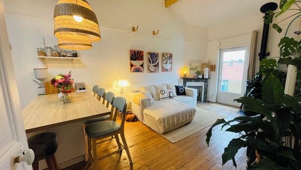 A cozy living room with a dining area, wooden flooring, a large plant, and a fireplace.