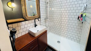 A bathroom with a white sink, wooden vanity, a mirror with a golden frame, and a shower area with white tiles.
