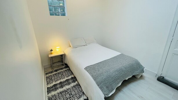 A small, single-bed room with a bedside table, a lamp, a window, and a patterned rug. - Charming family apartment in Basque house 10 minutes from beaches (Anglet)