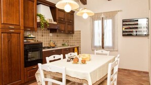 Una cucina con mobili in legno, un fornello, un tavolo da pranzo con sedie e una lampada a sospensione.