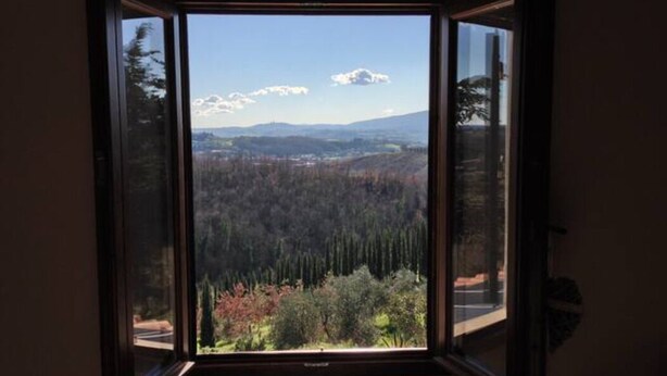 Una stanza con un'ampia finestra che si affaccia su un paesaggio boschivo e montagne in lontananza.