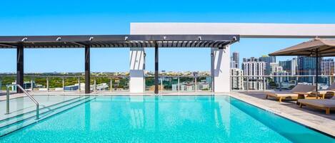 Una piscina en la azotea con vistas a la ciudad, una pérgola y sillas de descanso.