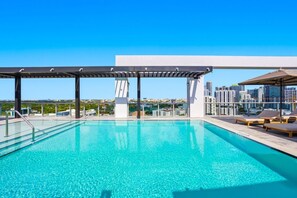 Ein Pool auf dem Dach mit Blick auf die Stadt, einer Pergola und Liegestühlen.