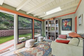 A room with a large window, a bookshelf, a sofa, and a painting. - South Oceanside Retreat 1.3 miles to the Beach! (Oceanside)