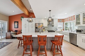 A modern kitchen with a large island, white cabinets, and wooden chairs. - South Oceanside Retreat 1.3 miles to the Beach! (Oceanside)