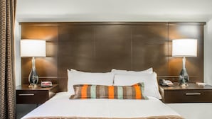 A hotel room with a large bed, two bedside tables, a nightstand, a lamp, a telephone, and a decorative pillow. - Accessible Queen Suite w/ Roll-In Shower (Okemos)