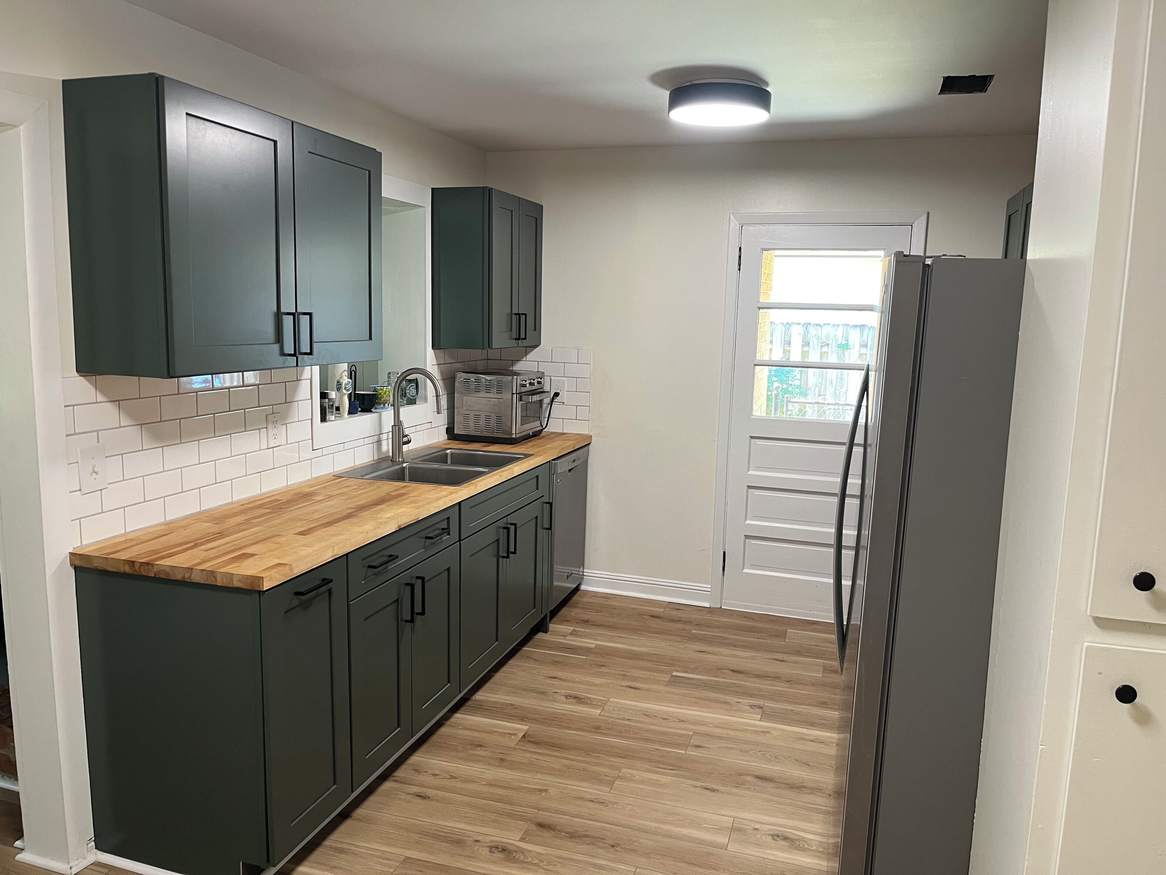 A kitchen with dark cabinets, a wooden countertop, a built-in microwave, and a stainless steel refrigerator.