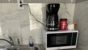 A kitchen with a double sink, a microwave, a coffee maker, a red Folgers coffee can, and a bottle of Dawn dish soap.