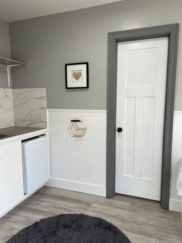 A kitchen with a white refrigerator, a marble backsplash, a white door, and a black rug.