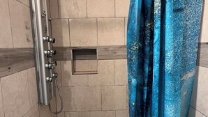 A shower with a white curtain, a handheld showerhead, and a drain in the floor.