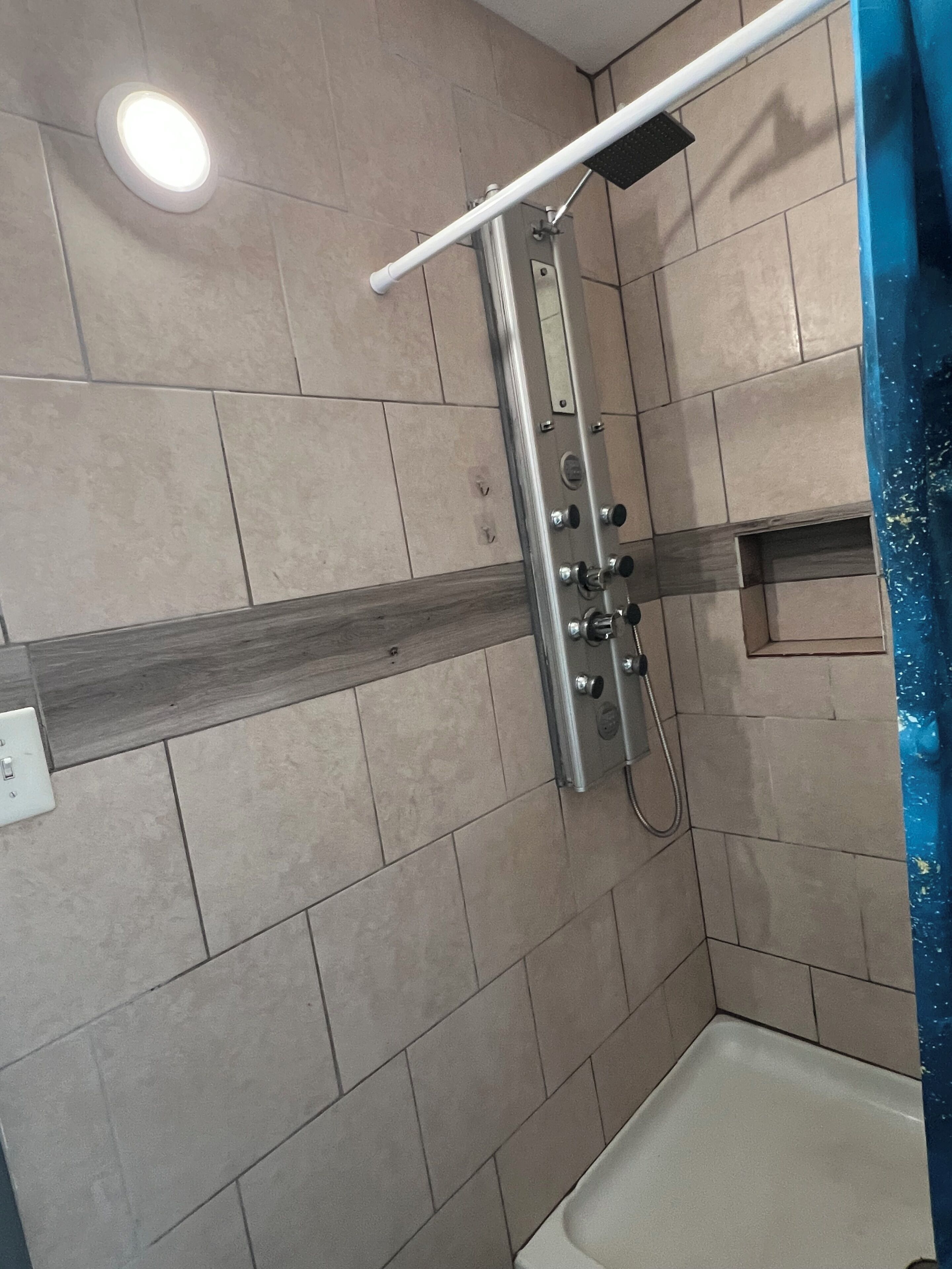 A shower area with tiled walls, a metal showerhead, and a white ceiling light.