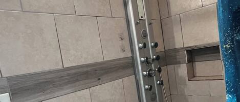 A shower area with tiled walls, a metal showerhead, and a white ceiling light.