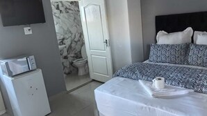 Ein Schlafzimmer mit einem Bett, einem an der Wand befestigten Fernseher, einer Mikrowelle, einem Kleiderschrank und einem durch eine offene Tür einsehbaren Badezimmer.