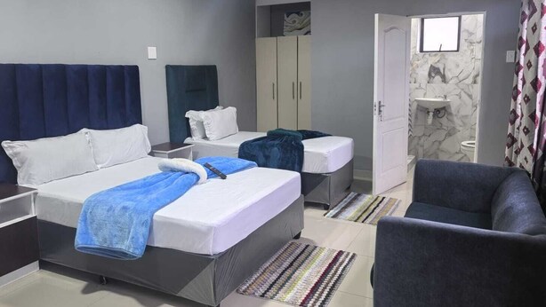 Ein Hotelzimmer mit Bett, zwei Nachttischen, einem Kleiderschrank, einem Badezimmer mit Waschbecken und Toilette sowie einem Sessel.