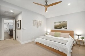 A bedroom with a bed, a ceiling fan, a wall-mounted artwork, and a bedside table with a lamp. - California Dream Beach House - Harbor Pointe (Carlsbad)