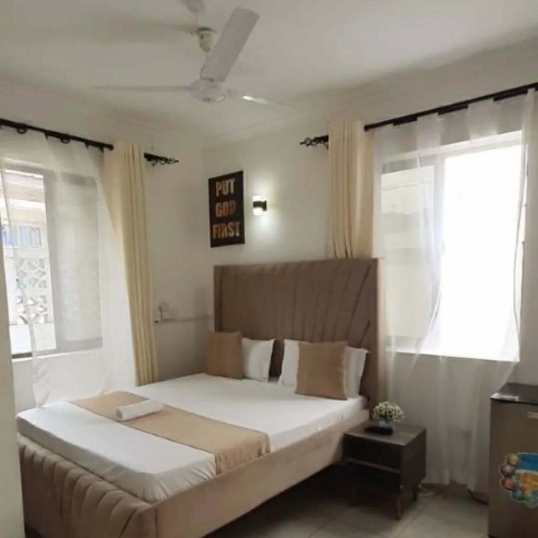 A bedroom with a bed, a nightstand, a ceiling fan, and a window with curtains.