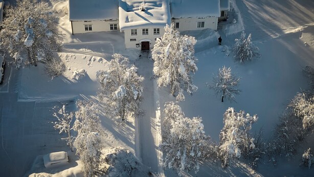 A snow-covered building with a central entrance, surrounded by snow-laden trees. - Lapland Nature & Health (Junosuando)