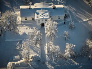 A snow-covered building with a central entrance, surrounded by snow-laden trees. - Lapland Nature & Health (Junosuando)