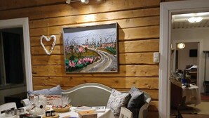 A dining area with a table set for two, a painting on the wall, and a heart-shaped decoration. - Lapland Nature & Health (Junosuando)
