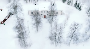 Une grande maison à deux étages, entourée d’arbres couverts de neige.
