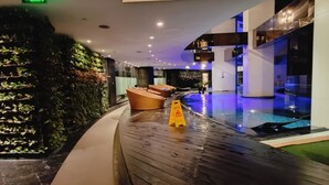 A modern indoor pool area with a curved wooden floor, a green exit sign, and a yellow caution sign. - Barefoot Sanctuary Stylish Condo Perfect for Staycations (Makati)