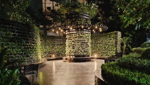 A circular seating area with a central column, surrounded by lush greenery and a patterned wall. - Barefoot Sanctuary Stylish Condo Perfect for Staycations (Makati)