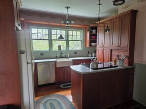 A kitchen with wooden cabinets, a stainless steel refrigerator, a sink, and a kettle on the counter. - Romantic Historic Riverside Escape in the Village of Greene (Greene)