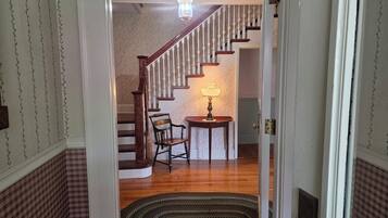 A staircase with a wooden handrail and white balusters, leading to a room with a patterned wallpaper and a table with a lamp.