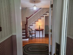 A staircase with a wooden handrail and white balusters, leading to a room with a patterned wallpaper and a table with a lamp.